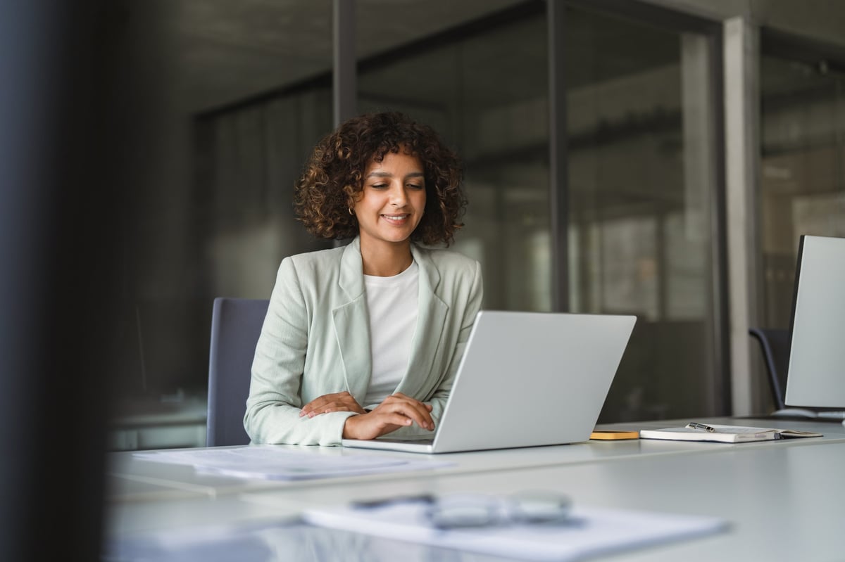 Young professional specialist latin hispanic businesswoman in suit working on laptop pc sitting at desk in office.