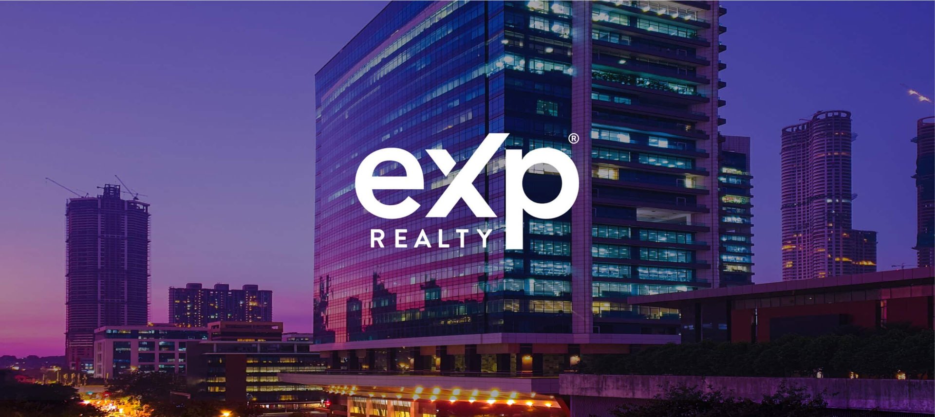 EXP Realty branded modern high-rise building illuminated at dusk with city skyline in the background