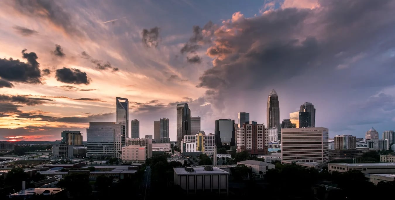 City skyline at sunset with tall buildings silhouetted against a dramatic pink and purple cloudy sky