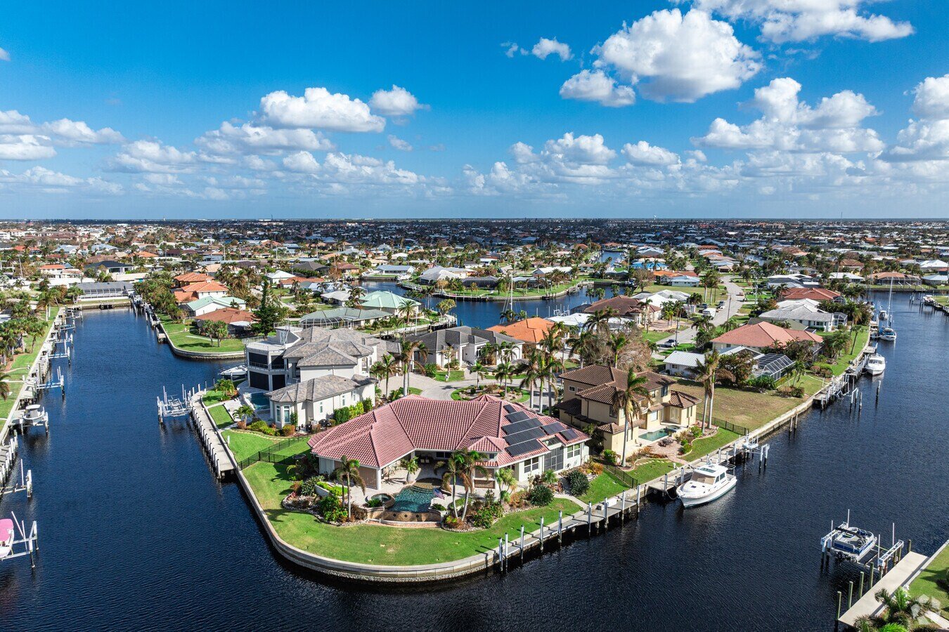 Aerial view of waterfront homes and boats on canals in a residential community under blue sky with white clouds