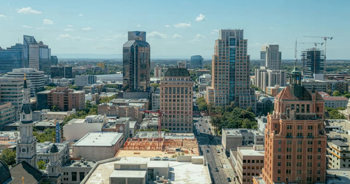 Aerial view of downtown cityscape with mixed architectural styles, skyscrapers, and construction sites under blue sky