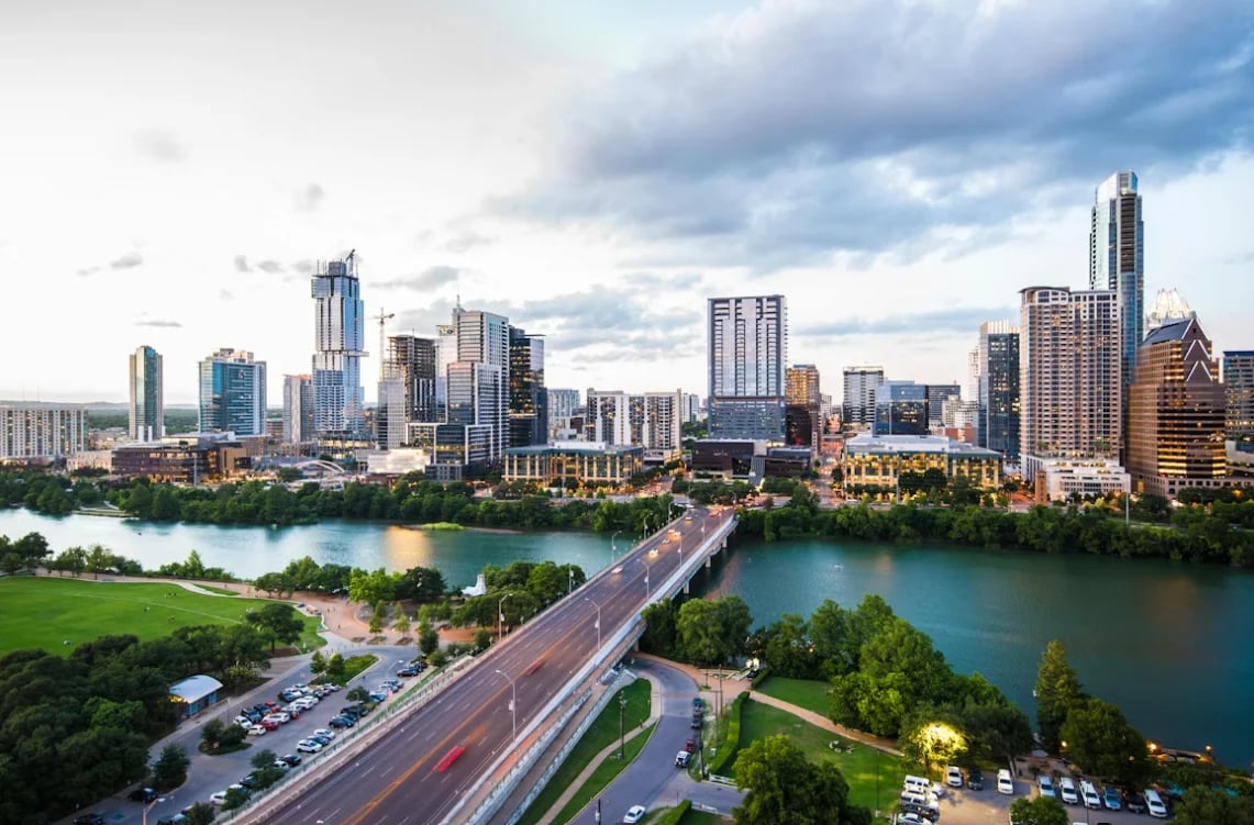 Austin, Texas skyline with downtown buildings overlooking Lady Bird Lake and a bridge during daytime with clouds