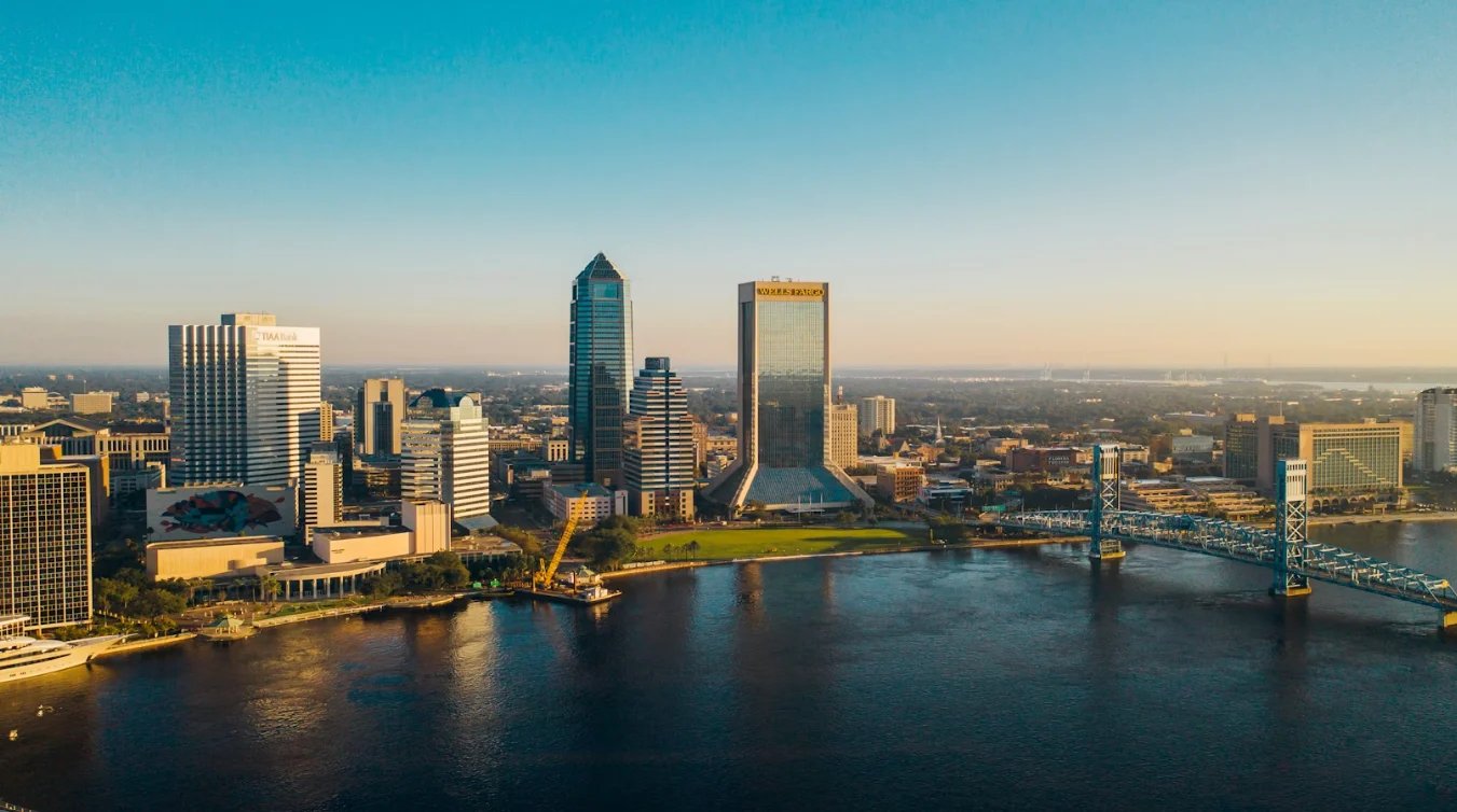 Aerial view of Jacksonville skyline at sunset with downtown buildings, river, and bridge