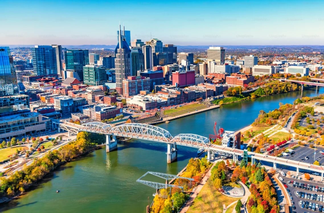 Aerial view of Nashville skyline with downtown buildings, river, and bridge on a sunny day