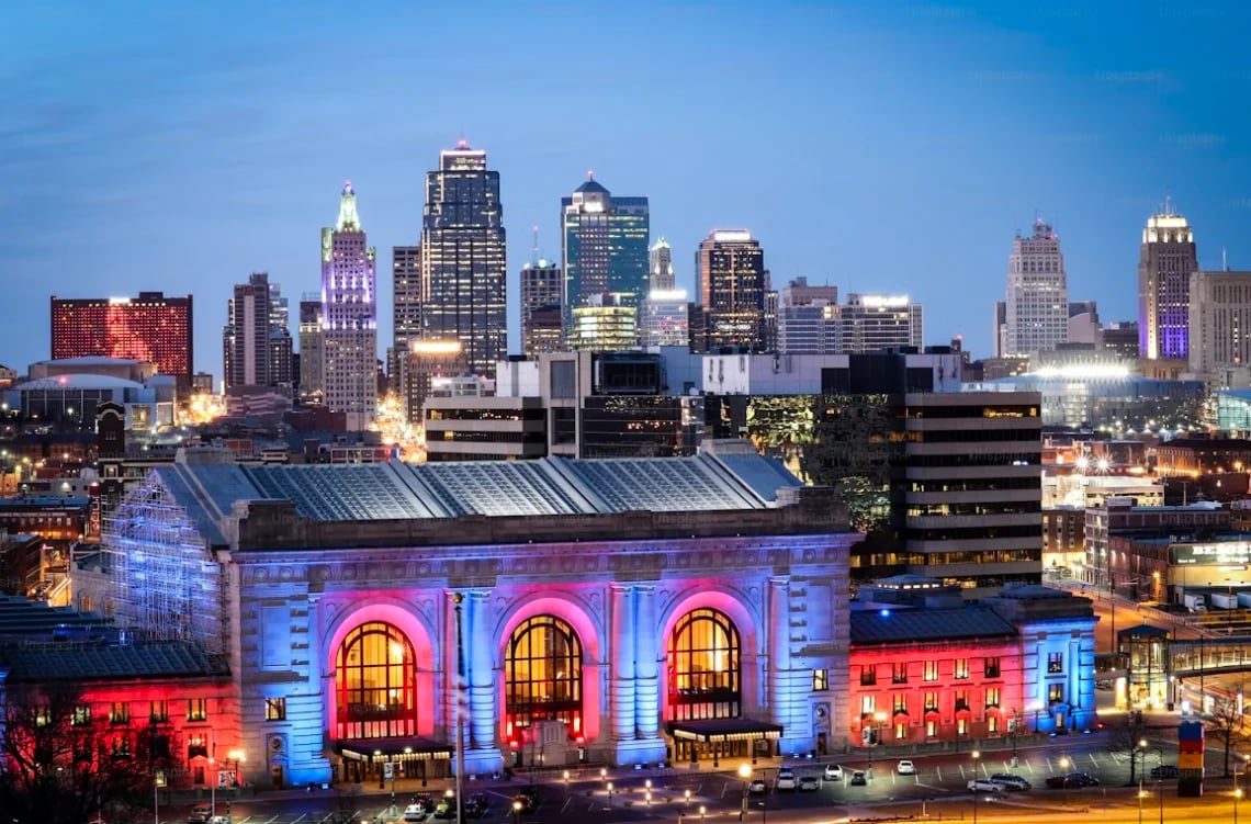Kansas City skyline at dusk with illuminated Union Station building featuring blue and red architectural lighting in foreground