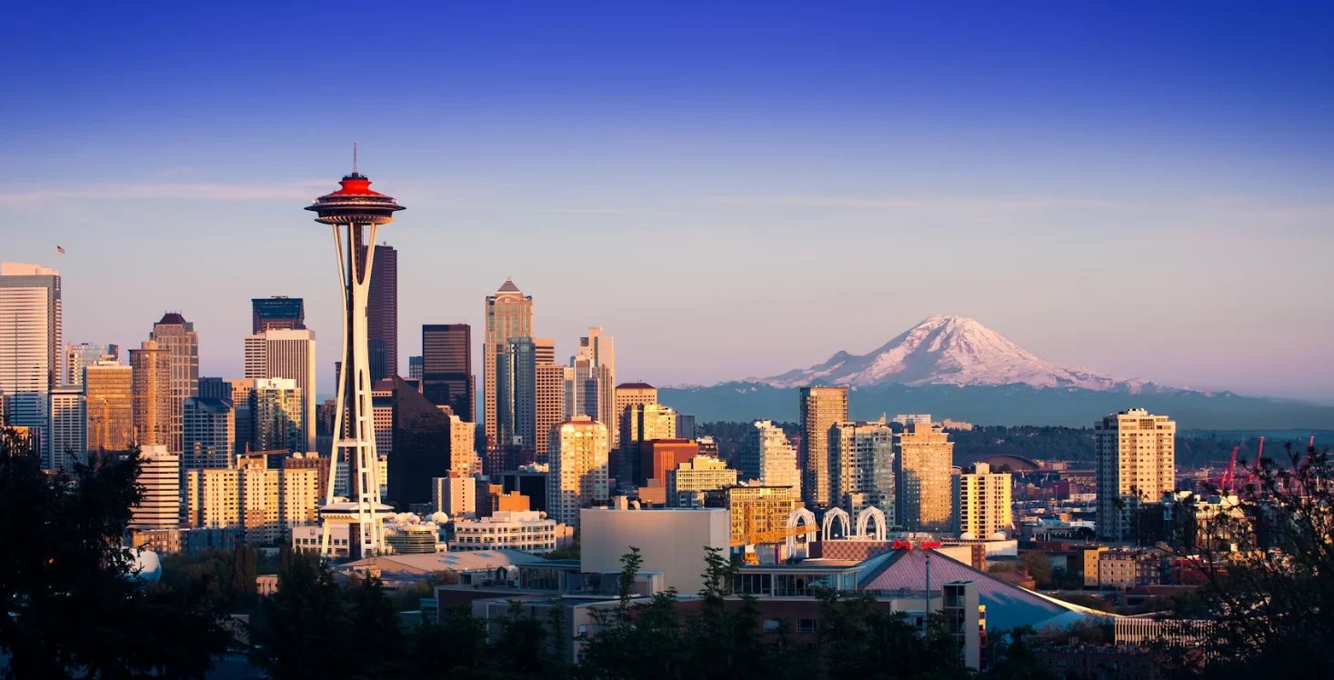 Seattle skyline at sunset with Space Needle and Mount Rainier in the background under clear blue sky