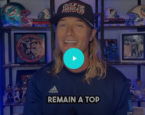 Person with long blonde hair wearing Gulf of America cap and Adidas Remain a Top hoodie, standing in front of shelves displaying memorabilia.