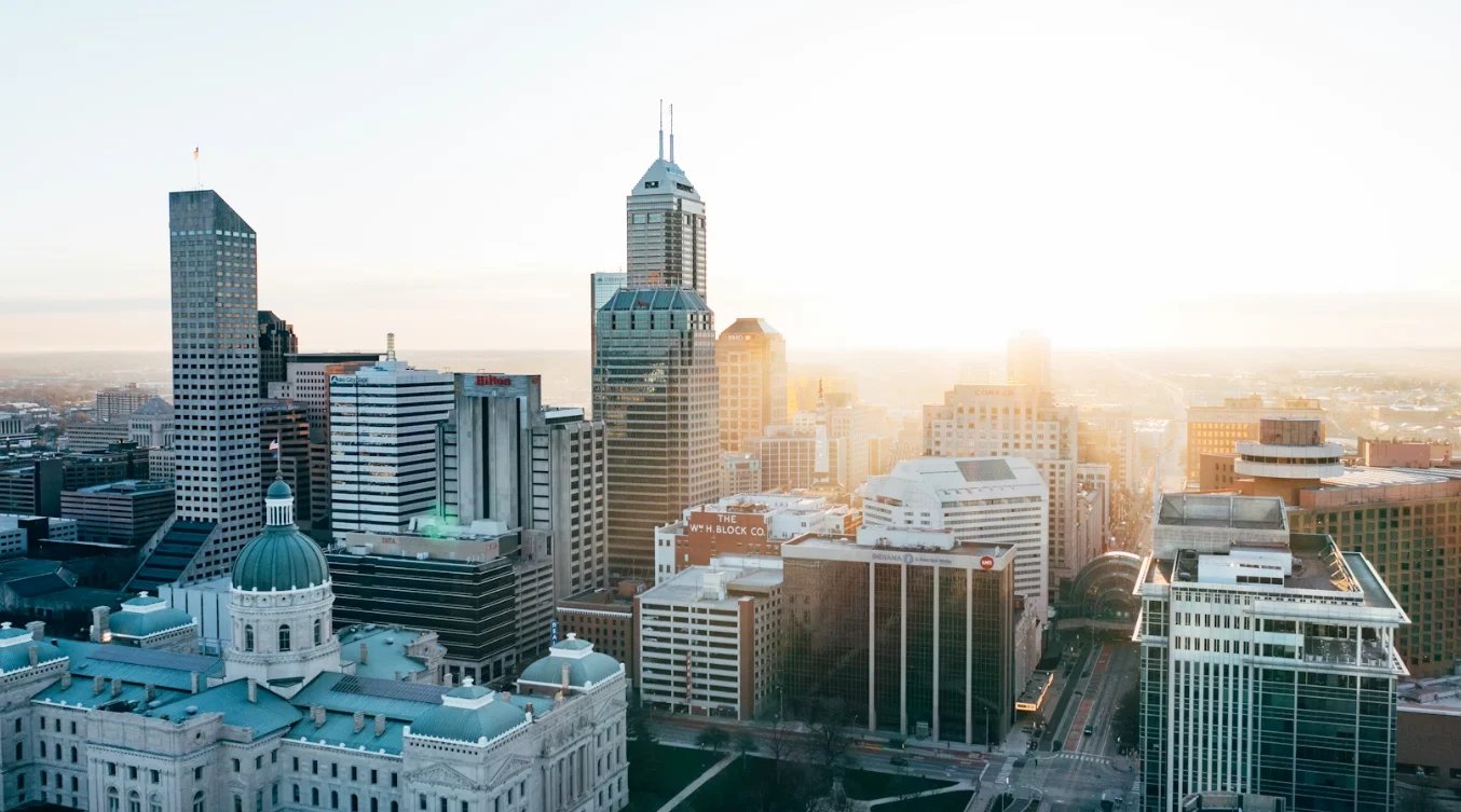 Aerial view of downtown Indianapolis skyline at sunset with tall buildings and a domed structure