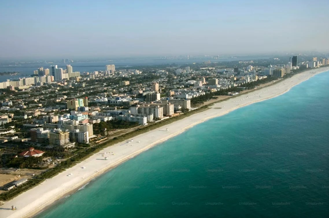 Aerial view of Miami Beach with turquoise ocean, sandy shoreline, and high-rise buildings of the city skyline in background