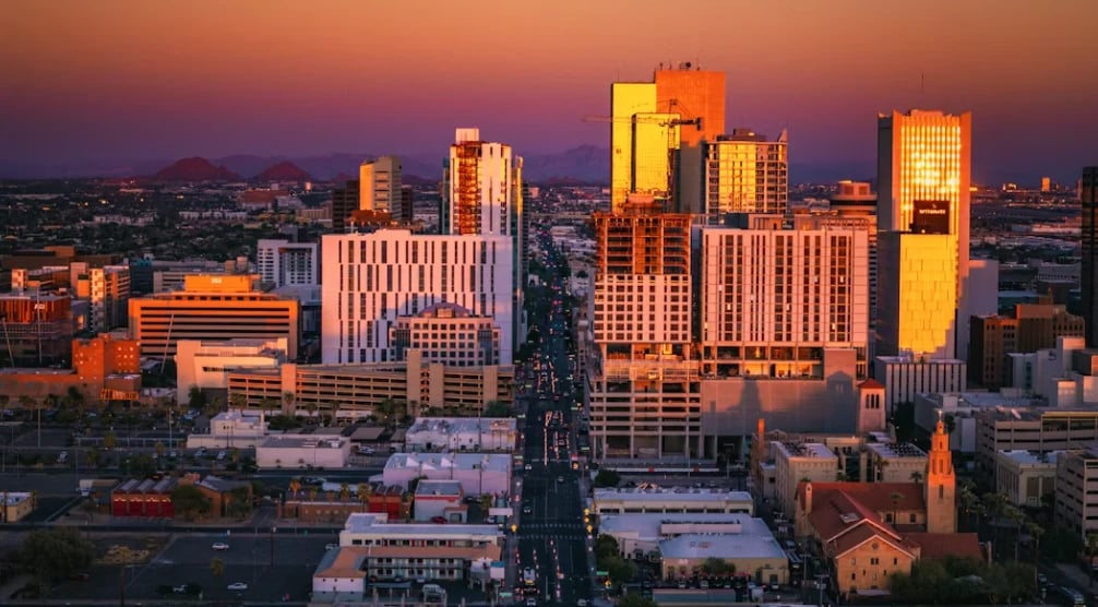 Downtown city skyline at sunset with illuminated skyscrapers glowing golden orange against a purple twilight sky